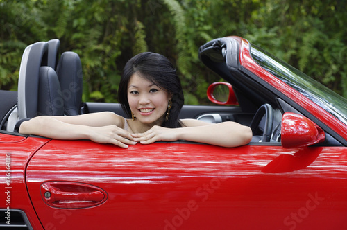 Woman sitting in red sports car, smiling at camera, portrait