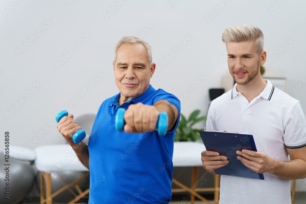 therapeut unterstützt einen senior beim training mit kleinen hanteln therapeut unterstützt einen senior beim training mit kleinen hanteln