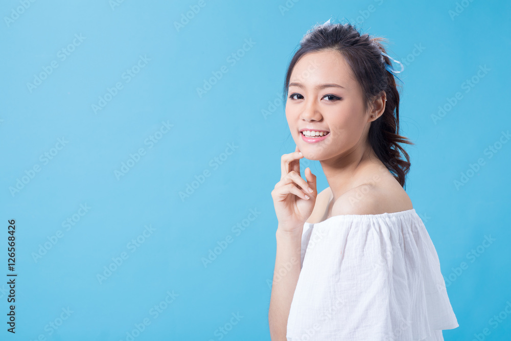 Asian cute young girl holding cosmetic product in white shirt showing her skin in light blue background Asian cute young girl holding cosmetic product in white shirt showing her skin in light blue background