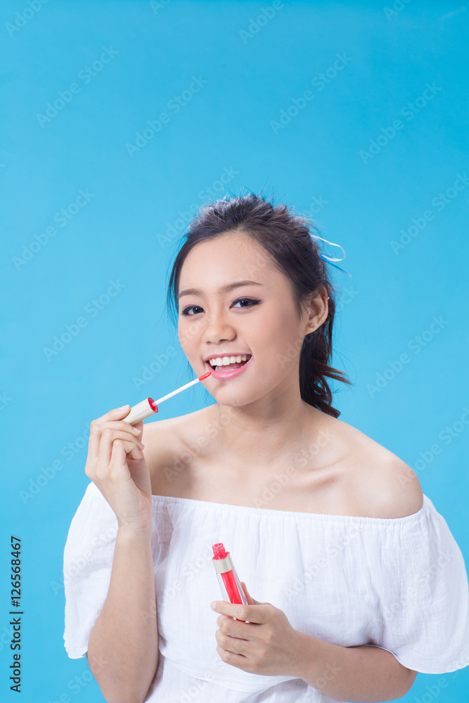 Asian cute young girl holding cosmetic product in white shirt showing her skin in light blue background Asian cute young girl holding cosmetic product in white shirt showing her skin in light blue background