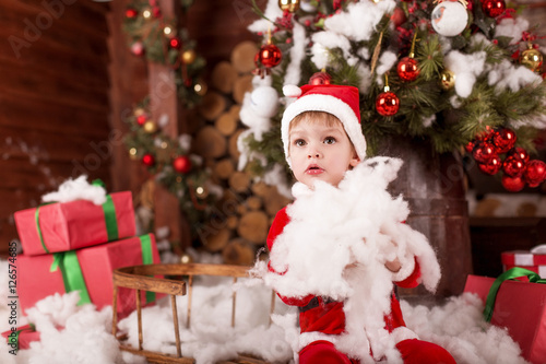 Little child (boy) in the costume of Santa Claus played with white snow near the Christmas tree with gifts © olyapon