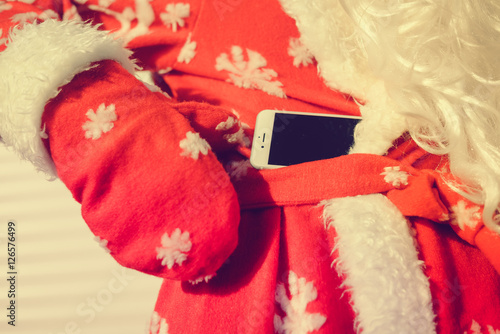 Close up on Santa Slaus using mobile phone in hands, copy space background photo