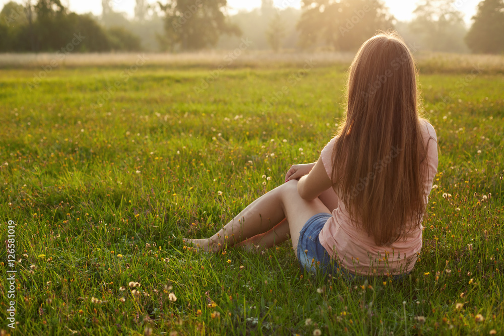 Fototapeta premium Back view of an attractive young woman with long dark hair sitti