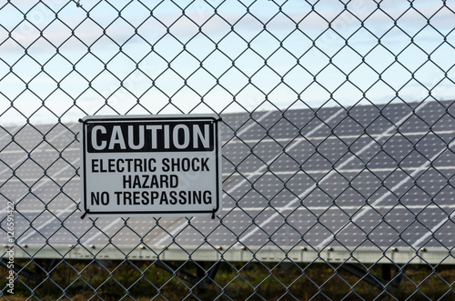 Solar panel array behind fence with caution sign
