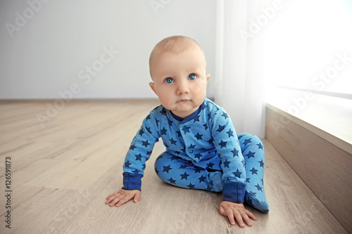 Adorable little baby sitting on wooden floor