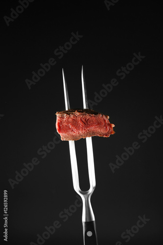 Fork with delicious steak piece on black background