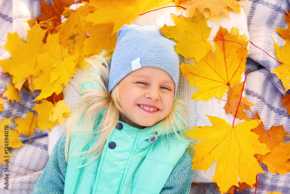 Cute little girl with yellow leaves lying on plaid, close up view