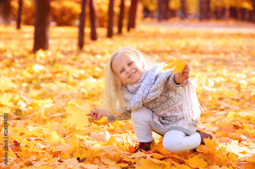 Cute little girl playing with leaves in autumn park on sunny day