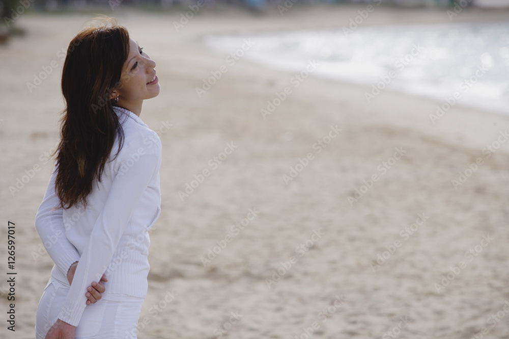 Young woman standing on beach, hands behind back, looking away Young woman standing on beach, hands behind back, looking away