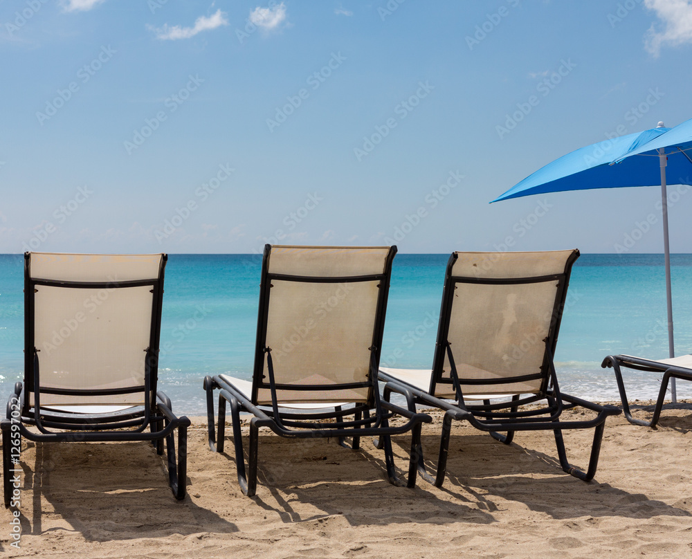Three beach loungers and umbrella on sand