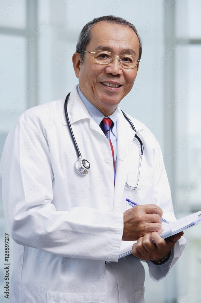 Doctor writing on medical chart, looking at camera