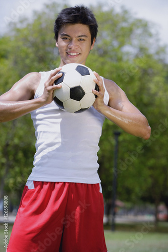 Young man holding soccer ball, looking at camera © Alexander