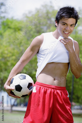 Young man with soccer ball, wiping chin with T shirt