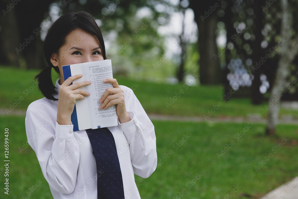 Young woman in school uniform, book covering face Young woman in school uniform, book covering face