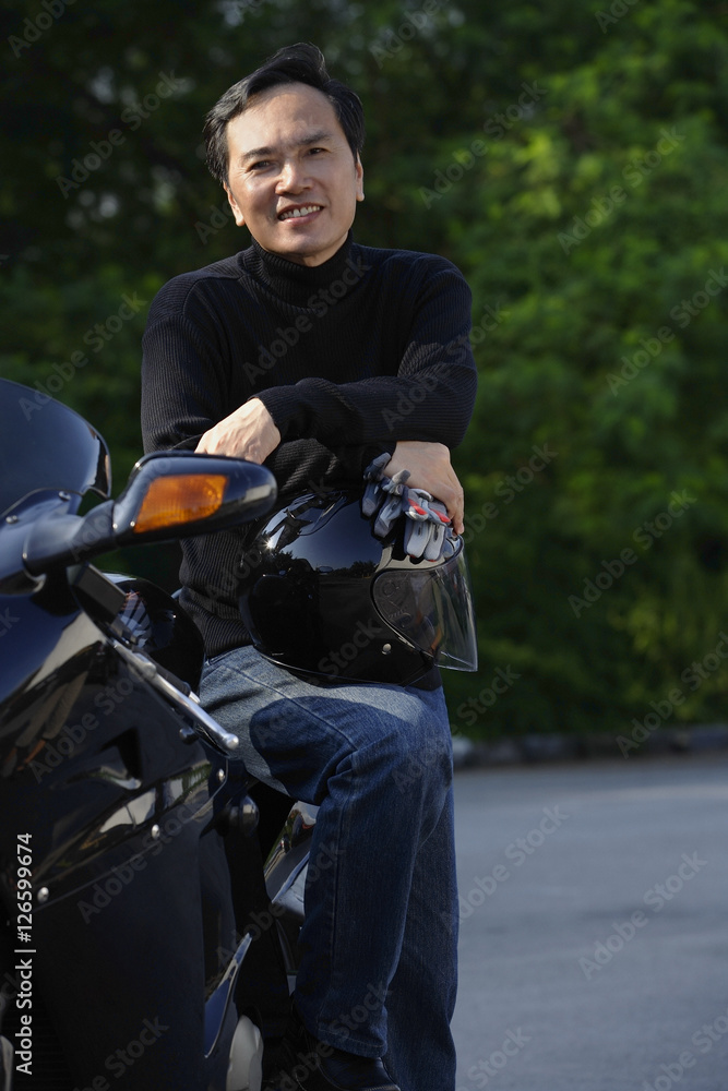 Man leaning on motorcycle, holding helmet, smiling at camera Man leaning on motorcycle, holding helmet, smiling at camera