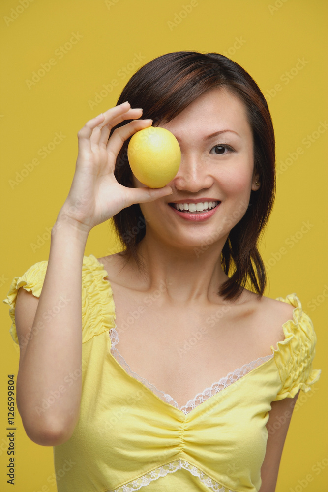 Young woman holding lemon over her eye, portrait Young woman holding lemon over her eye, portrait