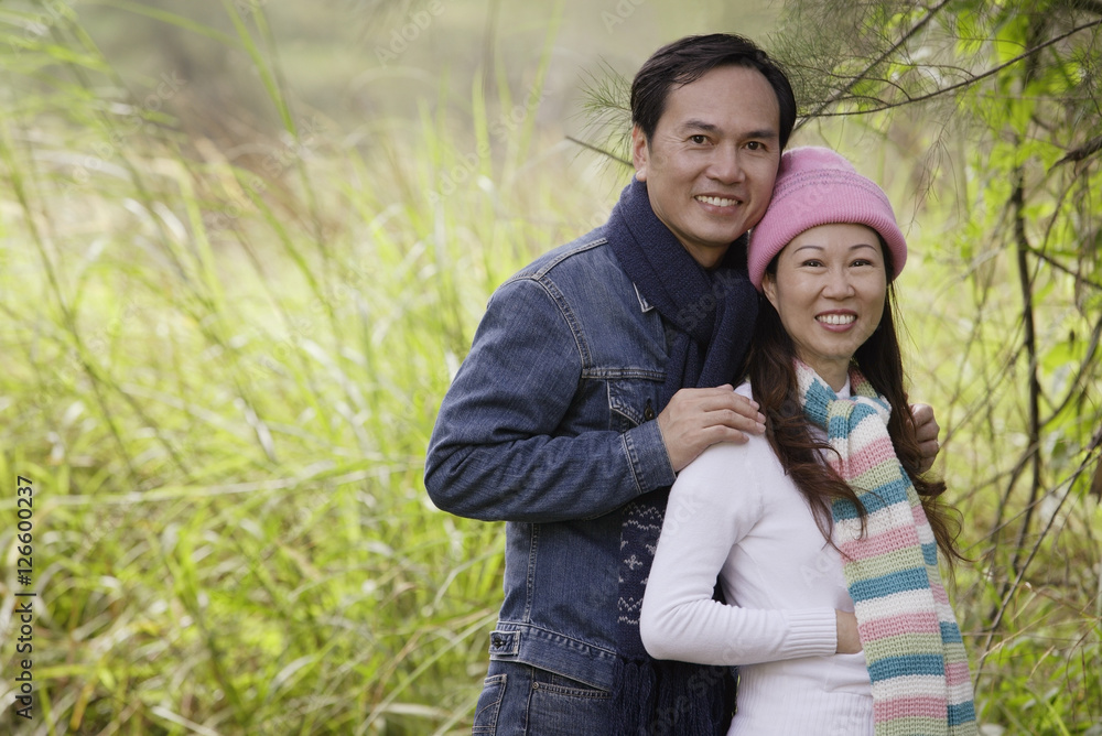 Man and woman wearing hat and scarves, standing outdoors in nature, smiling at camera Man and woman wearing hat and scarves, standing outdoors in nature, smiling at camera