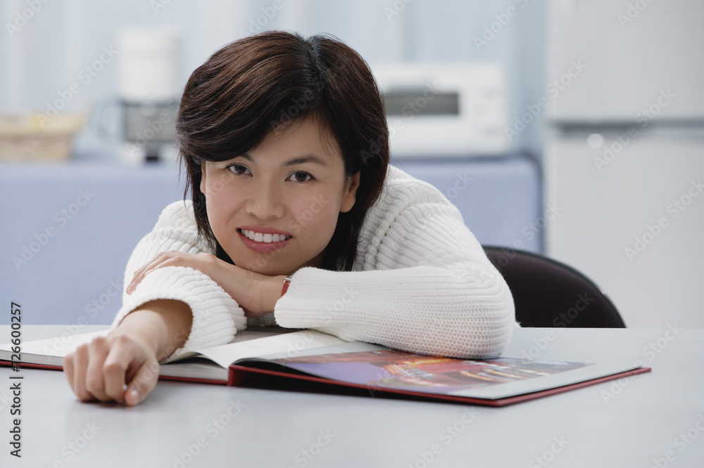 Woman leaning on table, book open in front of her, smiling at camera Woman leaning on table, book open in front of her, smiling at camera