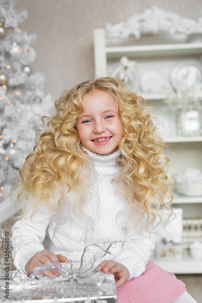 Portrait of smiling blonde little girl on a sofa with a gift box in Christmas Portrait of smiling blonde little girl on a sofa with a gift box in Christmas
