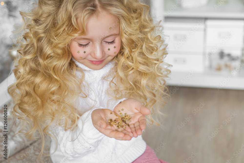 Portrait of pretty blonde little girl looks at a confetti at hands in Christmas Portrait of pretty blonde little girl looks at a confetti at hands in Christmas