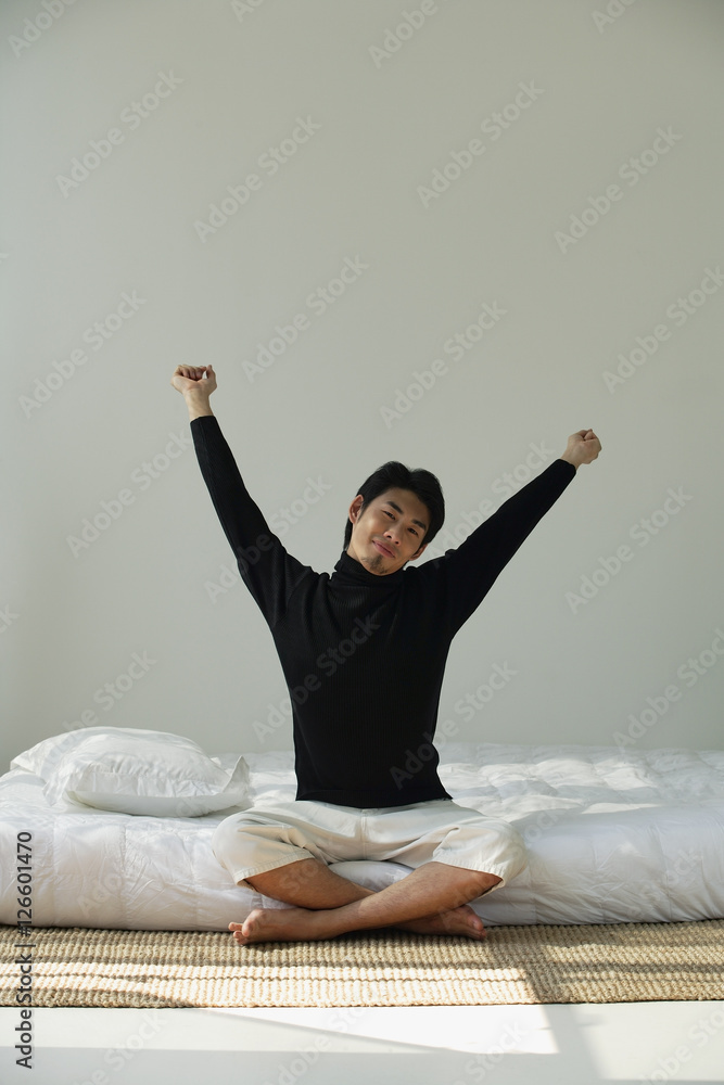 Young man sitting on bed, stretching arms