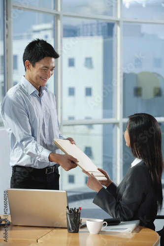 Картината върху платно Two colleagues smile at each other as they exchange documents