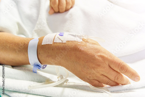 Closeup saline water line at the hand of patient on bed in hospital room, infusion line in a patients hand