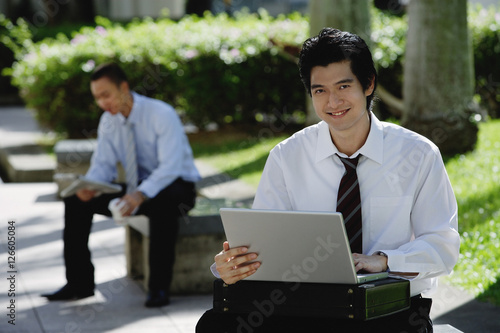 A man uses his laptop in the park while he looks at the camera