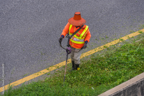 Public services worker cuts the grass along a road verge in Thailand.