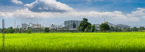 View of a factory in the middle of a green rice field. Factory pipes polluting air on a silent.