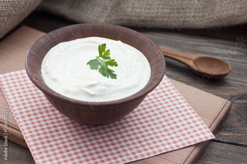 sour cream in a clay bowl on a table with fresh herbs