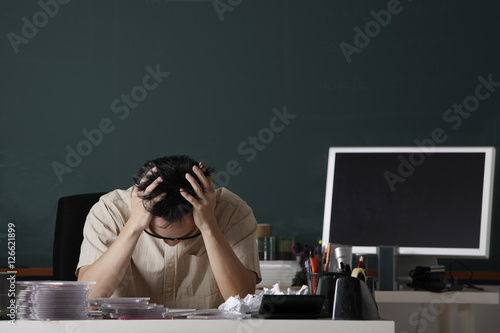 man sitting at desk in front of chalk board, stressed