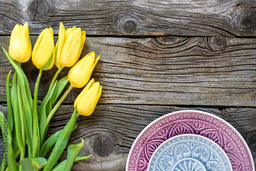 Fresh yellow tulip flowers with towel on ancient vintage wooden table  plates.