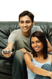 Couple sitting and facing forward, man holding remote control