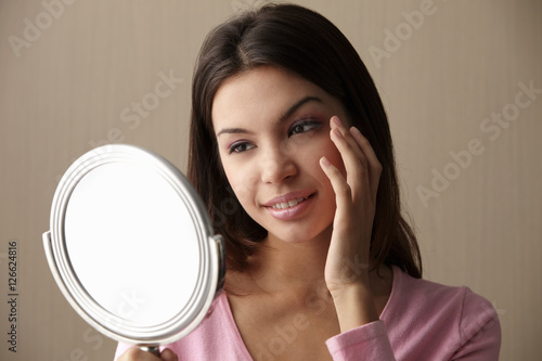 young woman looking at mirror touching her face