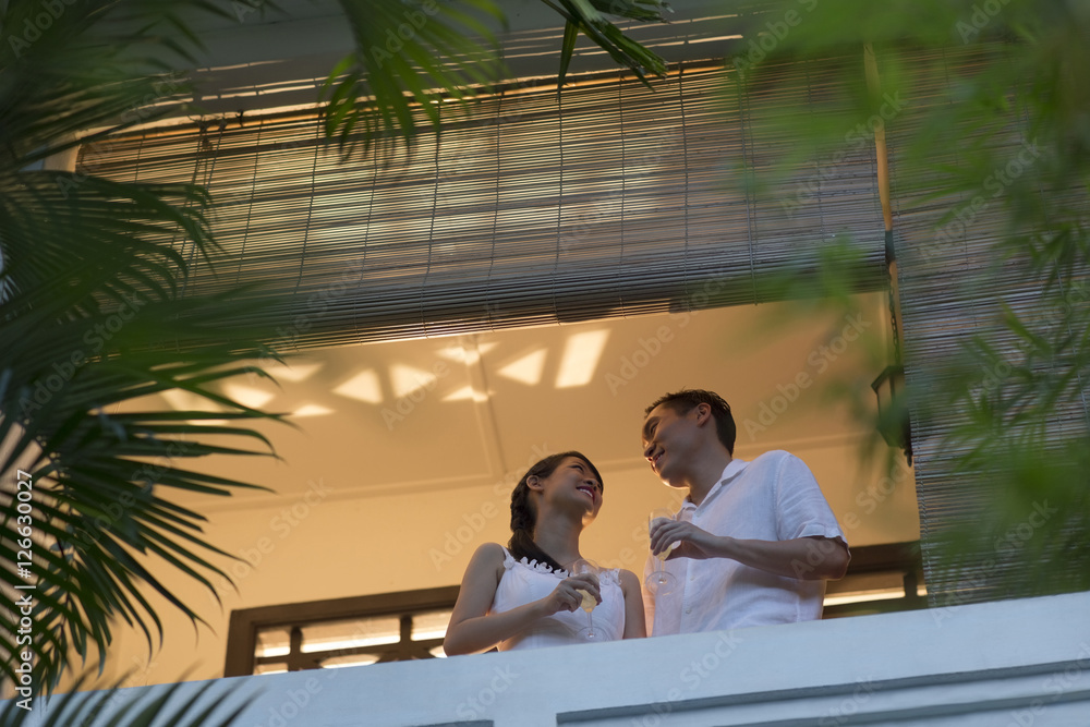Singapore, Mid-adult couple with champagne talking on balcony Singapore, Mid-adult couple with champagne talking on balcony