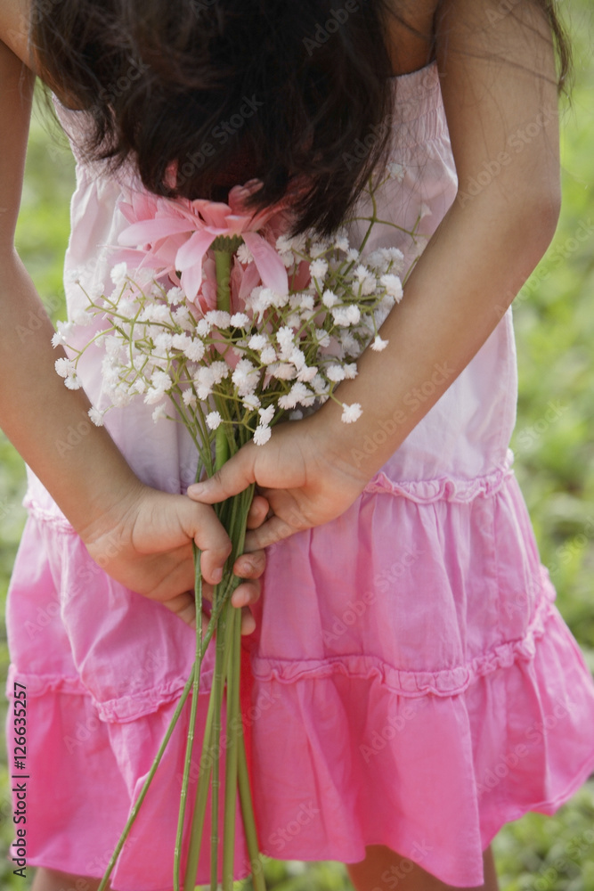 A small girl holds flowers behind her back