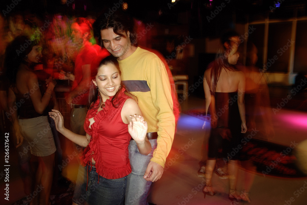Young adults dancing in night club, couple in the foreground