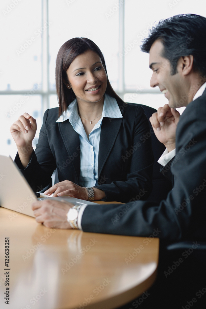 Businesswoman and businessman having a discussion, using laptop