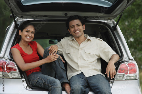 Young couple sitting in car boot smiling at camera