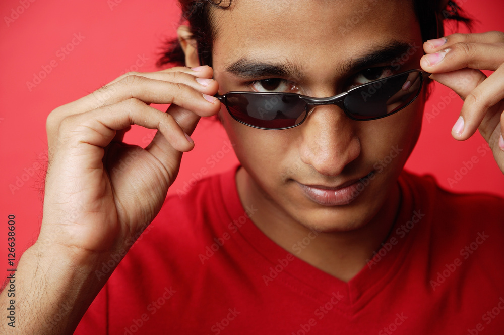 Man against red background, adjusting sunglasses, looking at camera Man against red background, adjusting sunglasses, looking at camera