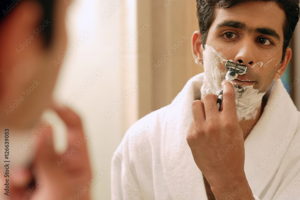 Man shaving his face, looking in mirror