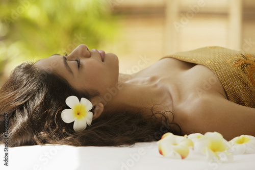 A woman lying down with frangipani flowers around her