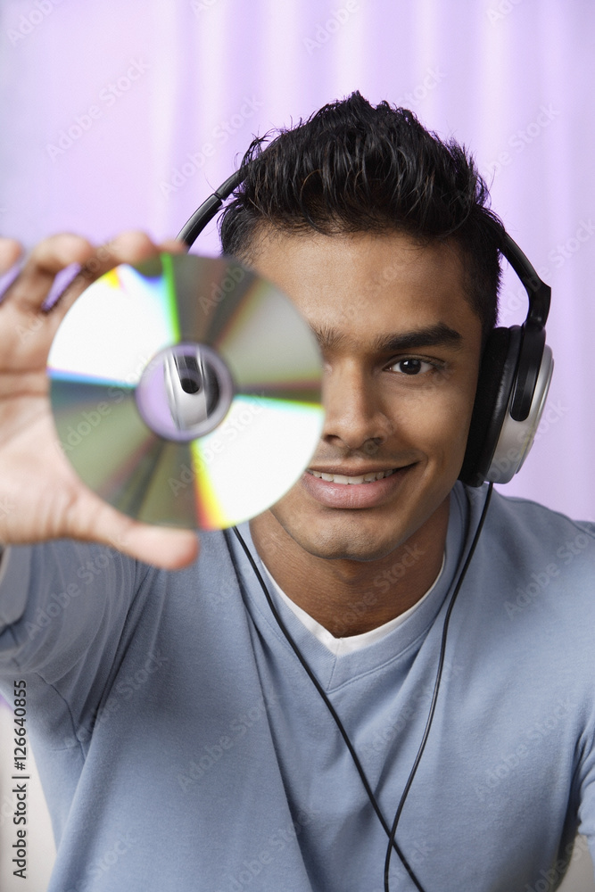 young man with headphones on, holding compact disc in front of him