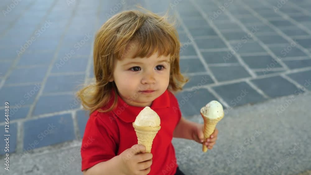 Curly-haired child toddler eating two ice cream on the street Curly-haired child toddler eating two ice cream on the street