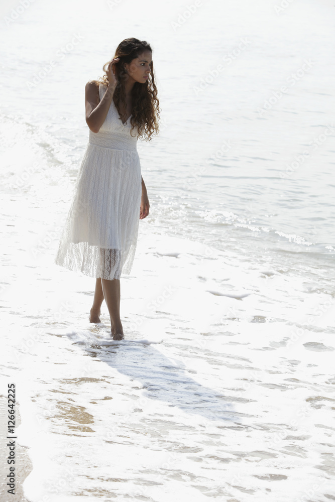 young woman wearing a white dress walking along the beach young woman wearing a white dress walking along the beach