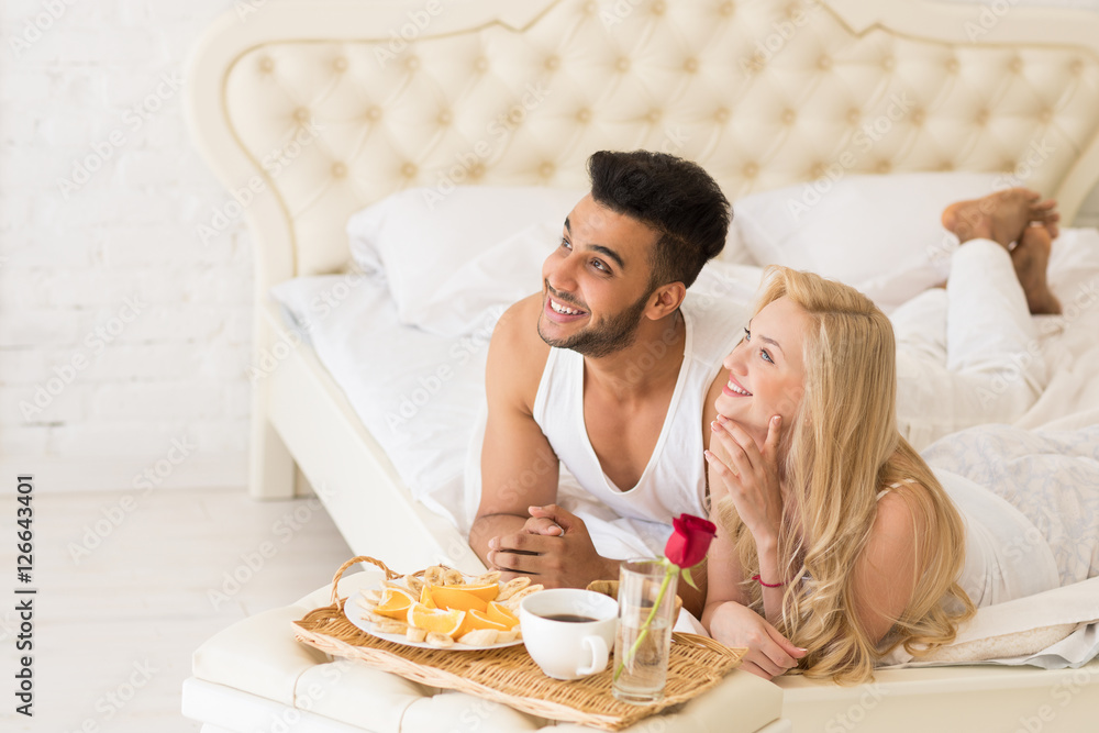 Young Couple Lying In Bed Eat Breakfast Morning With Red Rose Flower, Happy Smile Hispanic Man And Woman Lovers In Bedroom