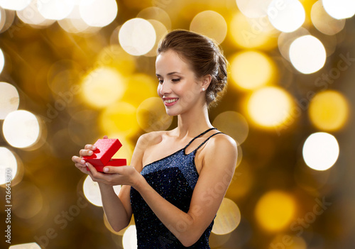 smiling woman holding red gift box over lights