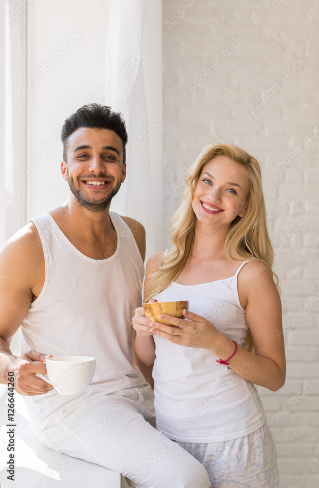 Young Beautiful Couple Stand Near Big Window, Drink Morning Coffee Cup, Happy Smile Hispanic Man And Woman Lovers Young Beautiful Couple Stand Near Big Window, Drink Morning Coffee Cup, Happy Smile Hispanic Man And Woman Lovers