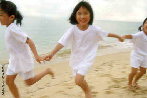 Children in white outfits running along the beach © Alexander